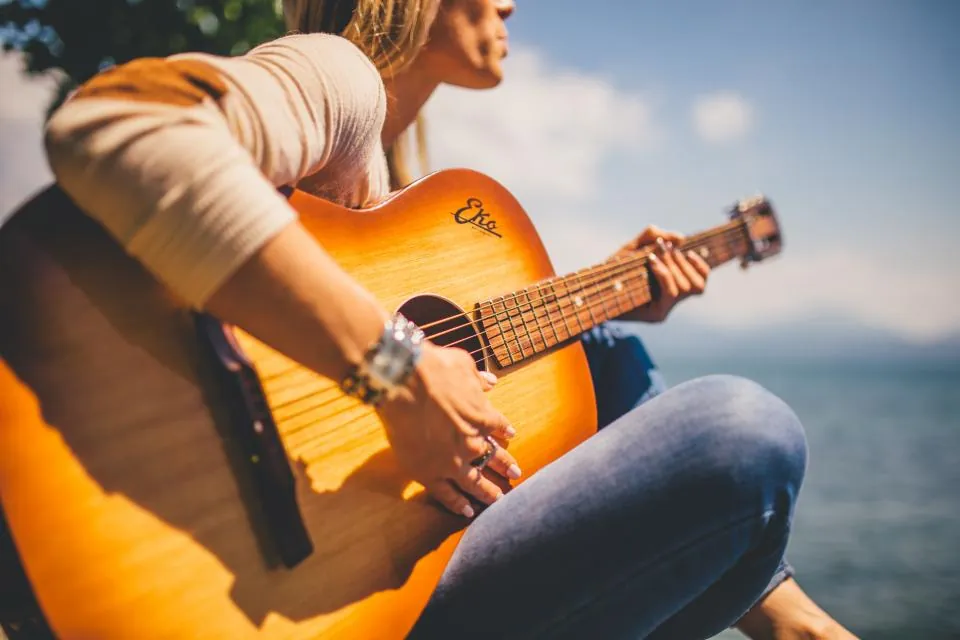 Seseorang memetik gitar akustik sambil duduk