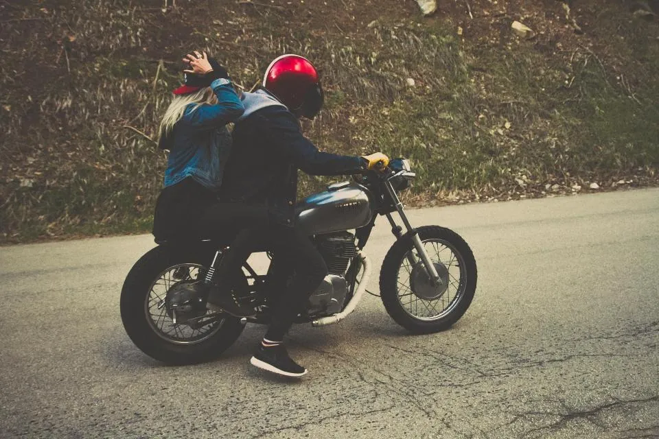 Dua orang berboncengan motor di jalan aspal yang sepi